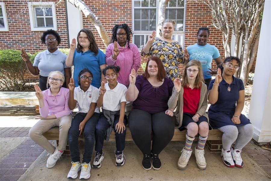  Ten girl scouts and their troop leader smile to camera while holding up 3 fingers.